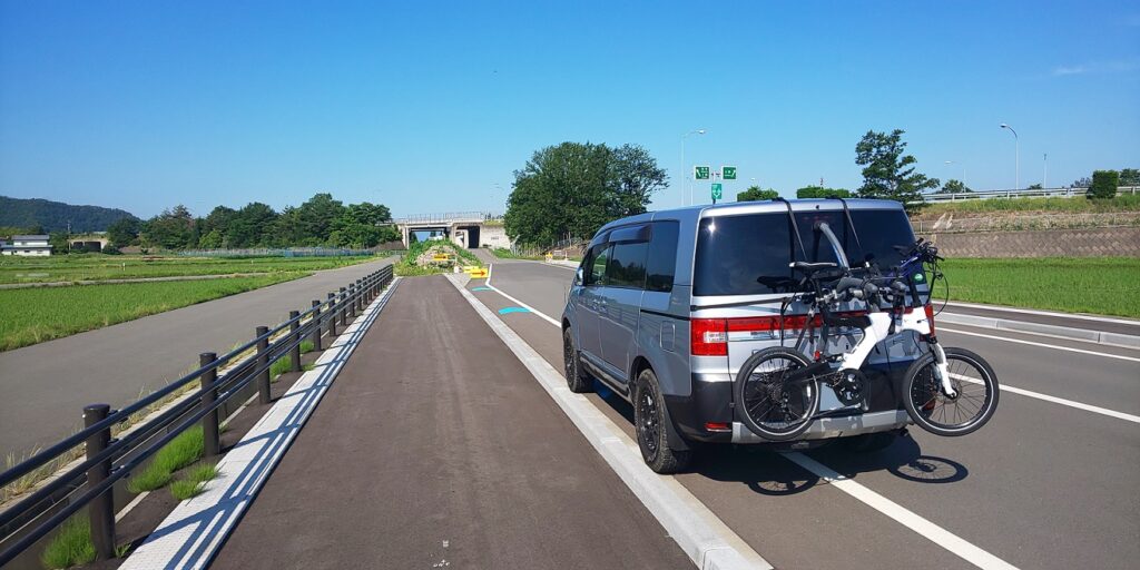 背面にサイクルキャリアを装着して電動自転車のBESV PS1を積載したデリカD:５が、道路わきに停車している。